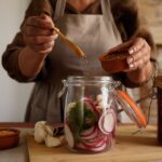 Hands preparing pickled vegetables in a jar, capturing a rustic and organic lifestyle.